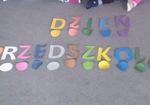 Napis Dzień Przedszkolaka ułożony z kolorowych literek na szarym dywanie.